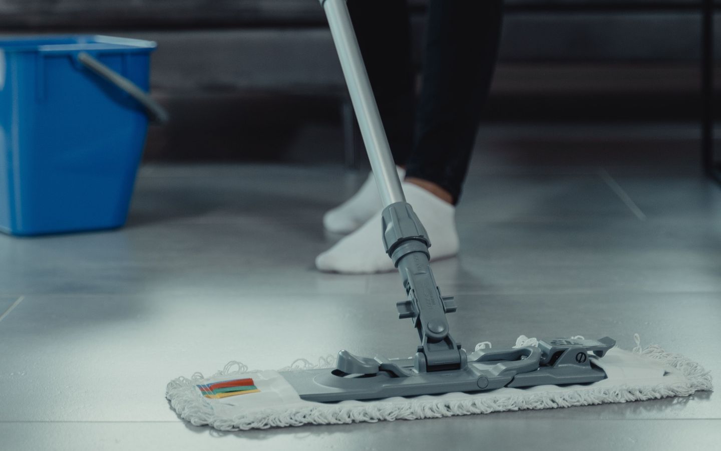 An operative cleaning a hard floor with a flat mop and a bucket.