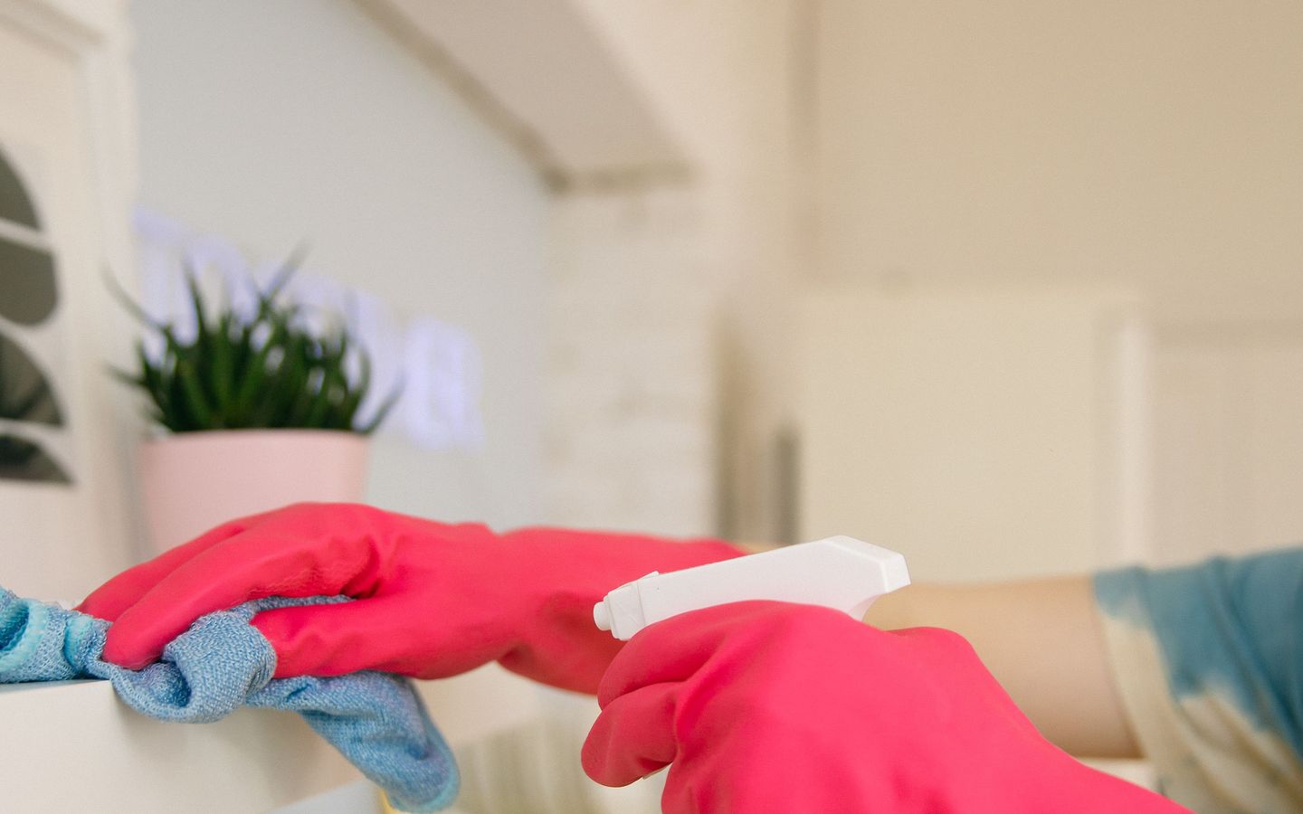 Gloved hands wiping a surface with a cloth and a trigger spray.